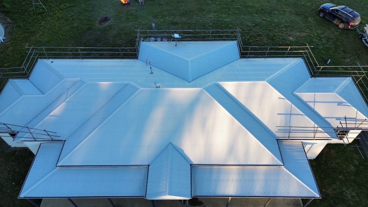 Aerial view of a large rural home with a pale corrugated metal hip roof and edge protection around it