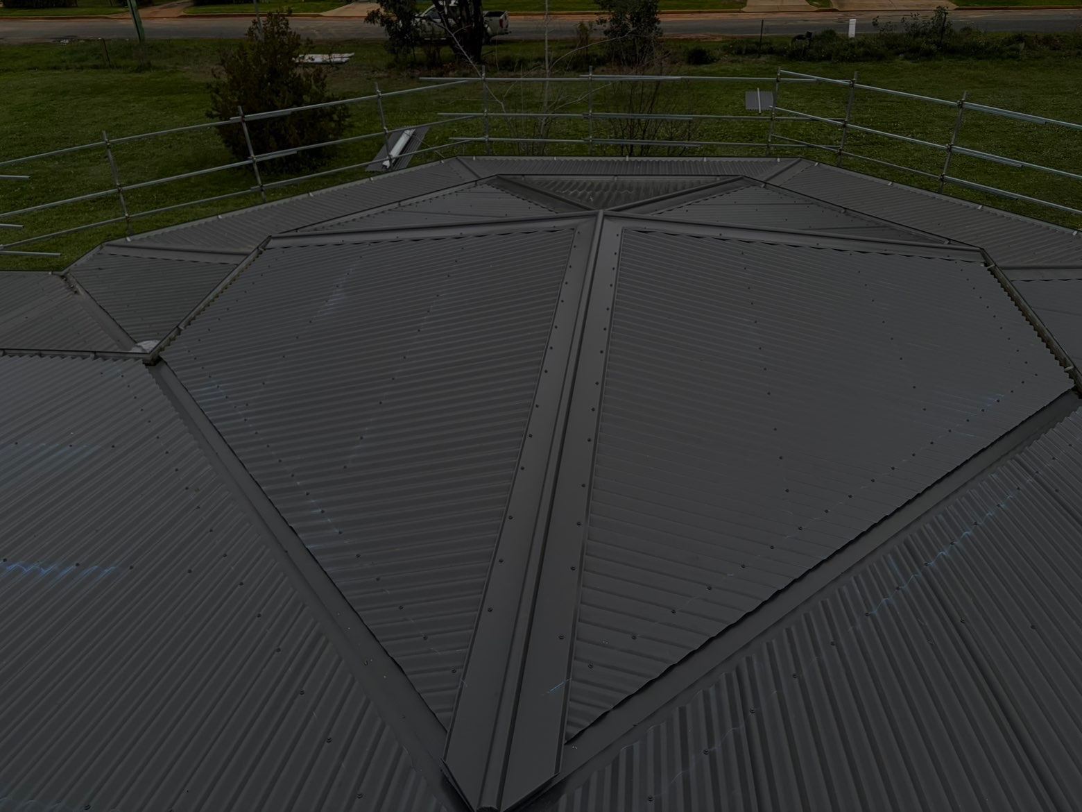 Several hips converging on a charcoal corrugated metal roof, with edge protection around the roof