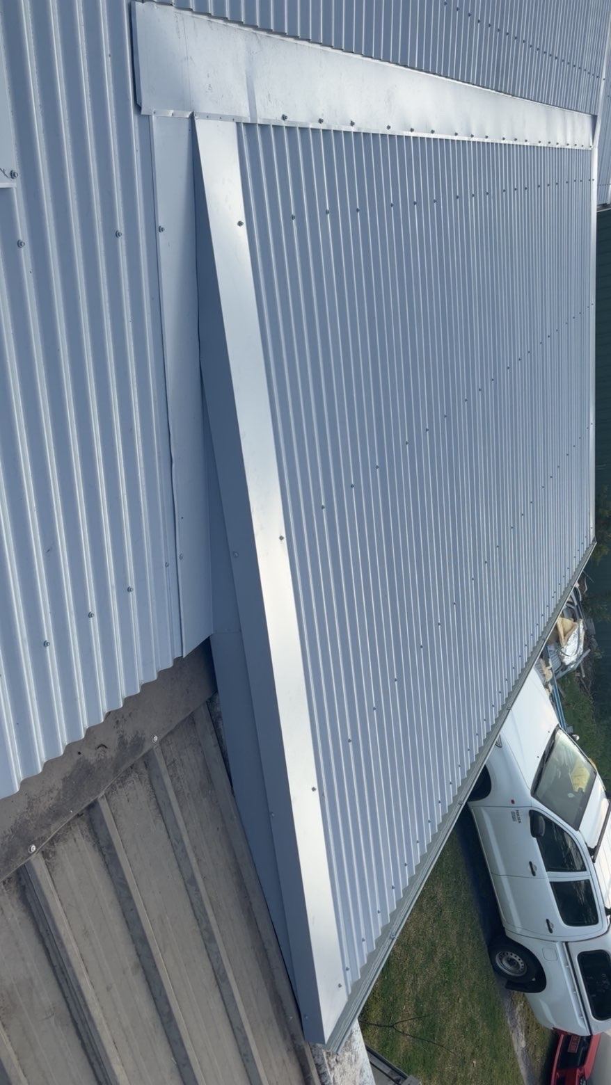 New corrugated metal sheets meeting an existing roof, with a long flashing along the join, seen from above