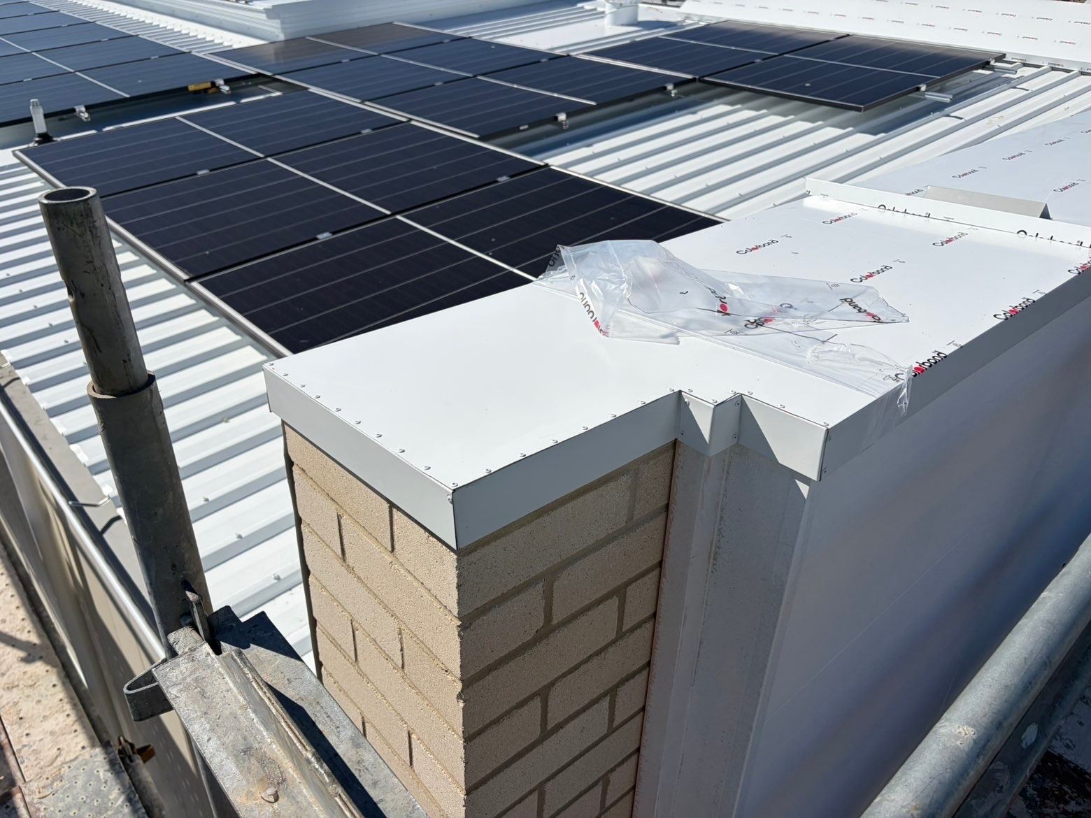 White metal capping over a brick pier with its protective film still on, beside a metal roof carrying solar panels