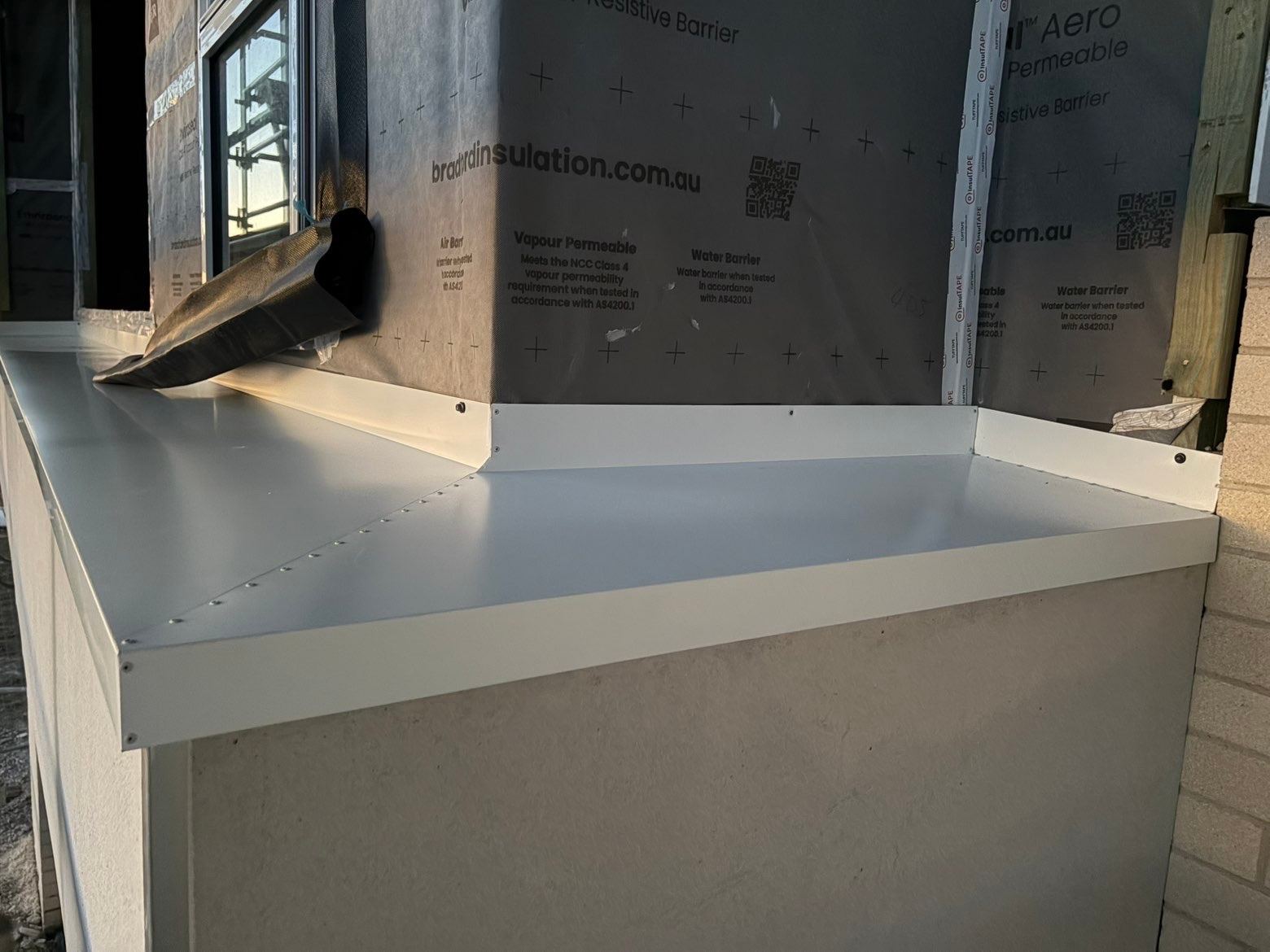 White folded metal flashing capping a wall on a house under construction, with building wrap on the wall above